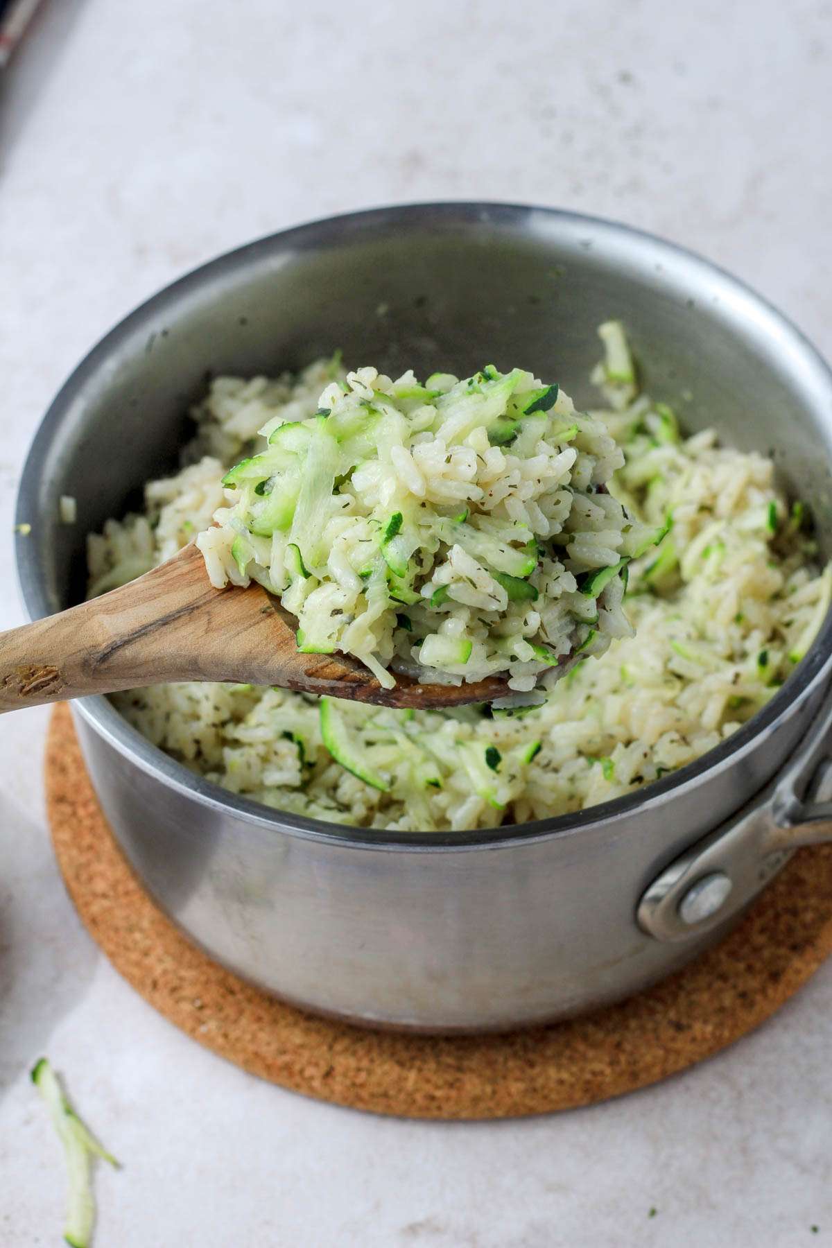 A wooden spoon with a scoop of seasoned vegan zucchini rice hovering over a saucepan of zucchini rice.