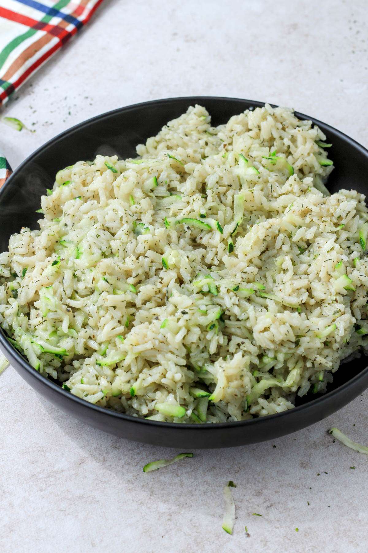 A black bowl piled high with vegan seasoned zucchini rice on a cream counter.