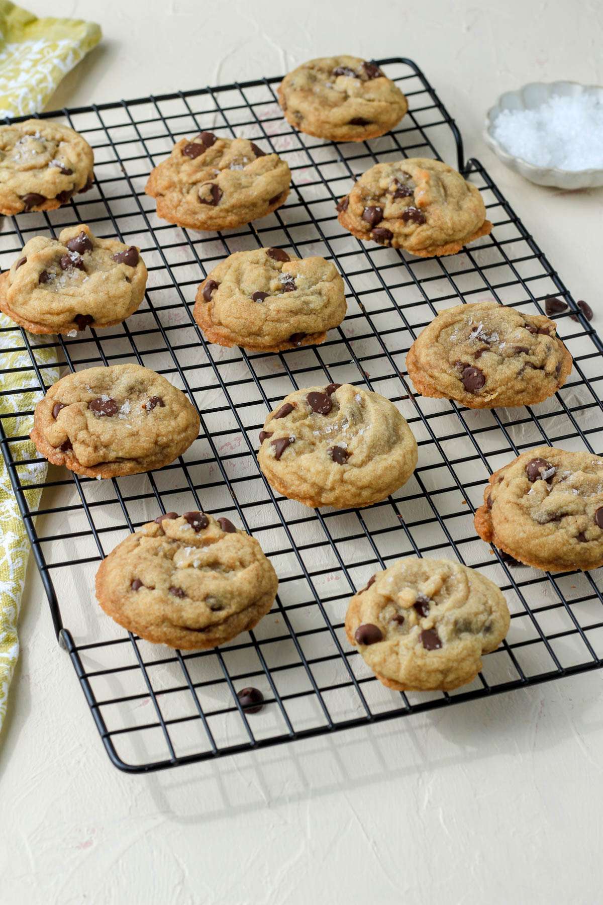 A black cooling rack on a cream counter with a dozen chocolate chip coconut oil cookies.