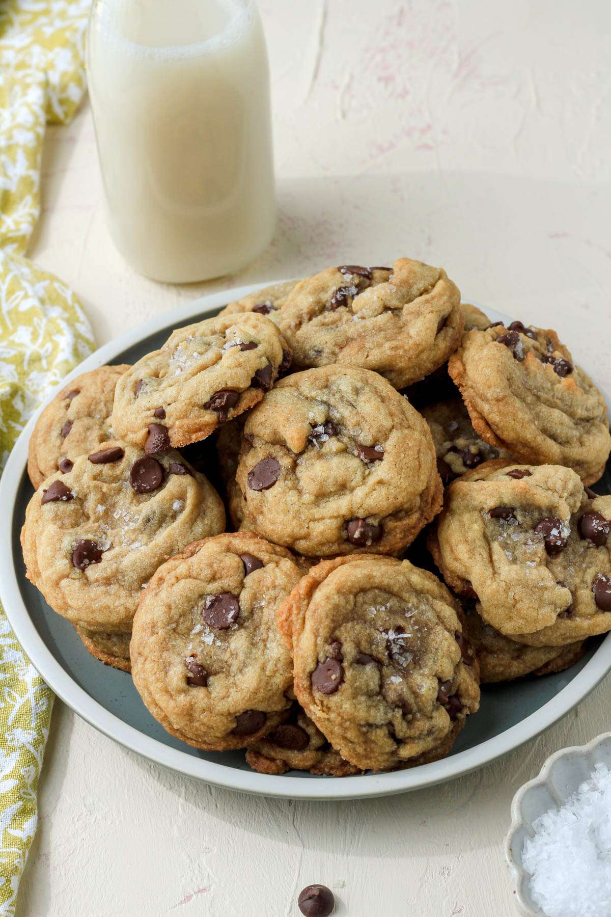 A green plate with a cream rim topped with chocolate chip coconut oil cookies with a jug of non-dairy milk in the back left.