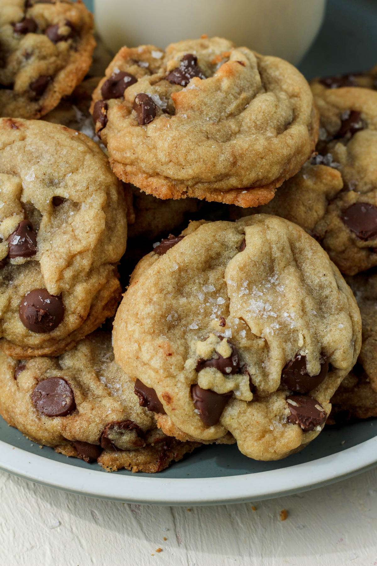 A green plate with a cream rim topped with coconut oil chocolate chip cookies in front of a jar of non-dairy milk.