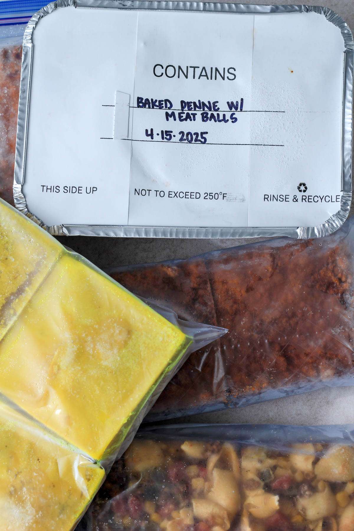 A top down image of a pan of baked penne surrounded by bags of frozen meals.