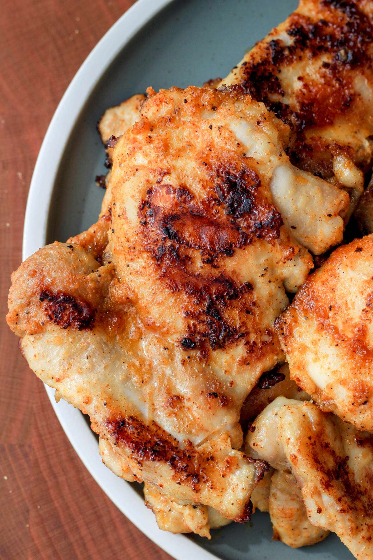 The left side of a green plate topped with juicy chicken thighs cooked on a grill pan.