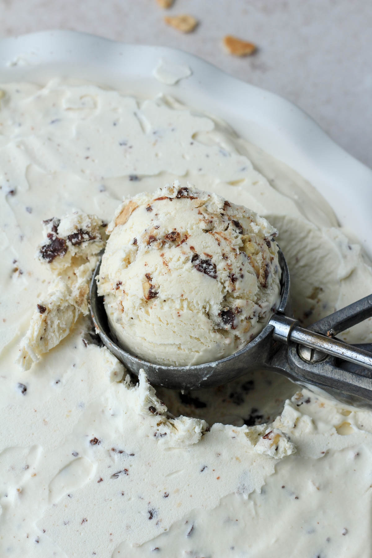 A silver ice cream scoop with a scoop of vegan no churn drumstick ice cream in a white pie pan.