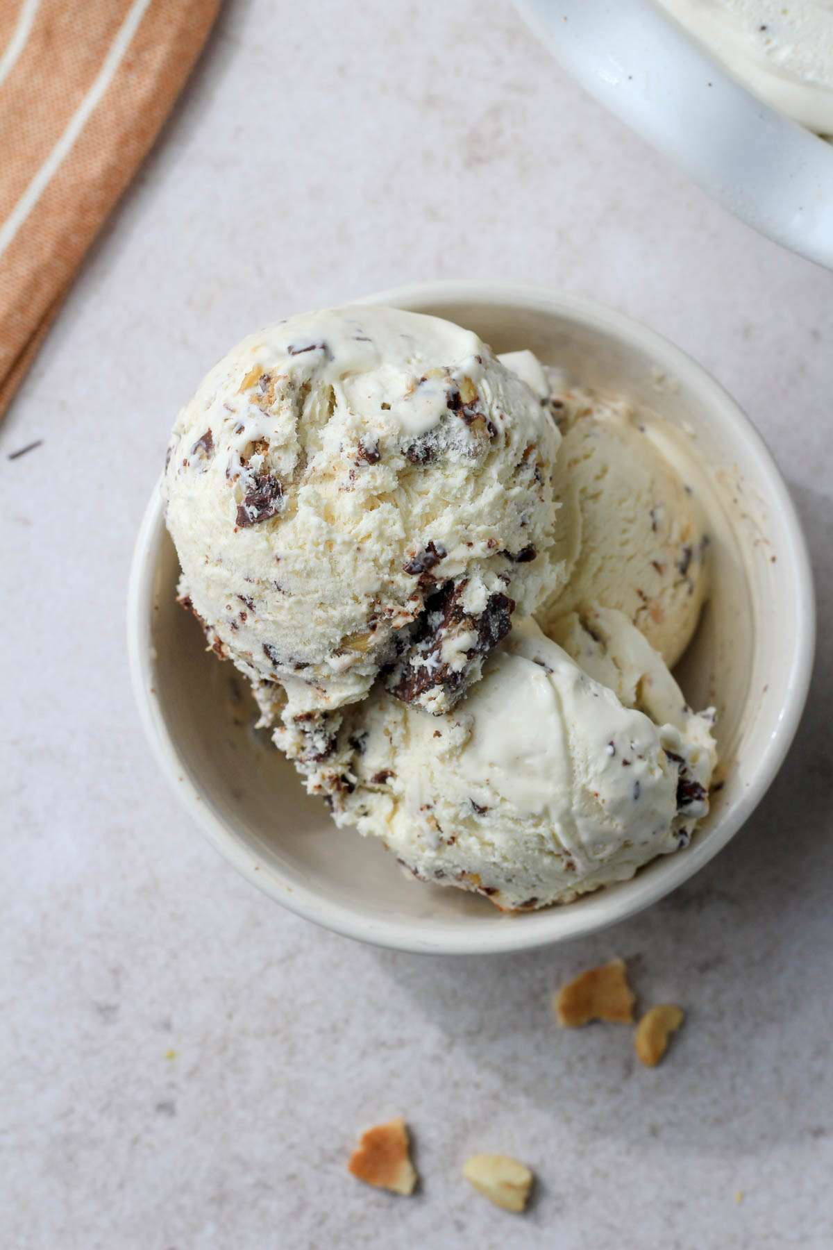 A cream bowl filled with scoops of dairy-free no churn drumstick ice cream on a tan counter.