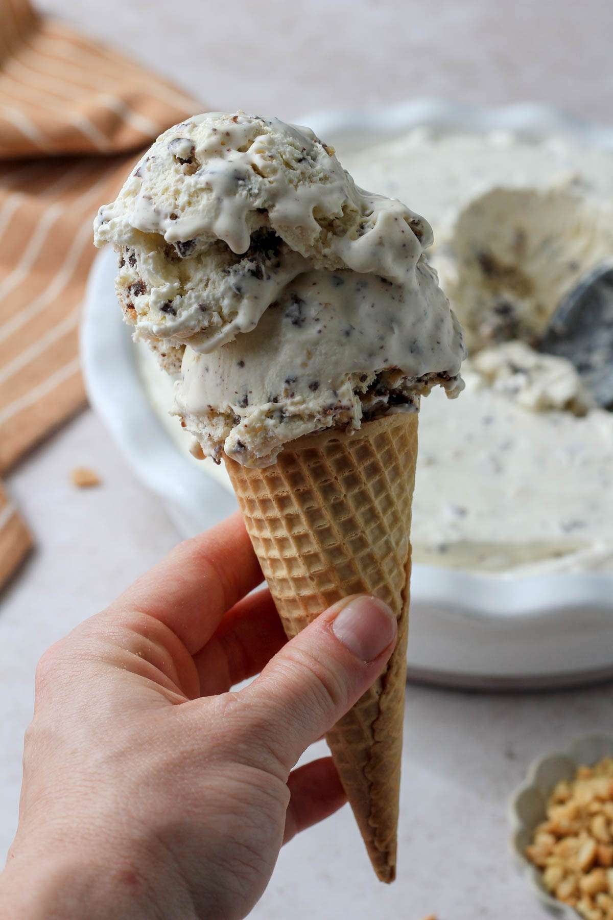 A hand with a sugar cone topped with scoops of dairy-free no churn drumstick ice cream.