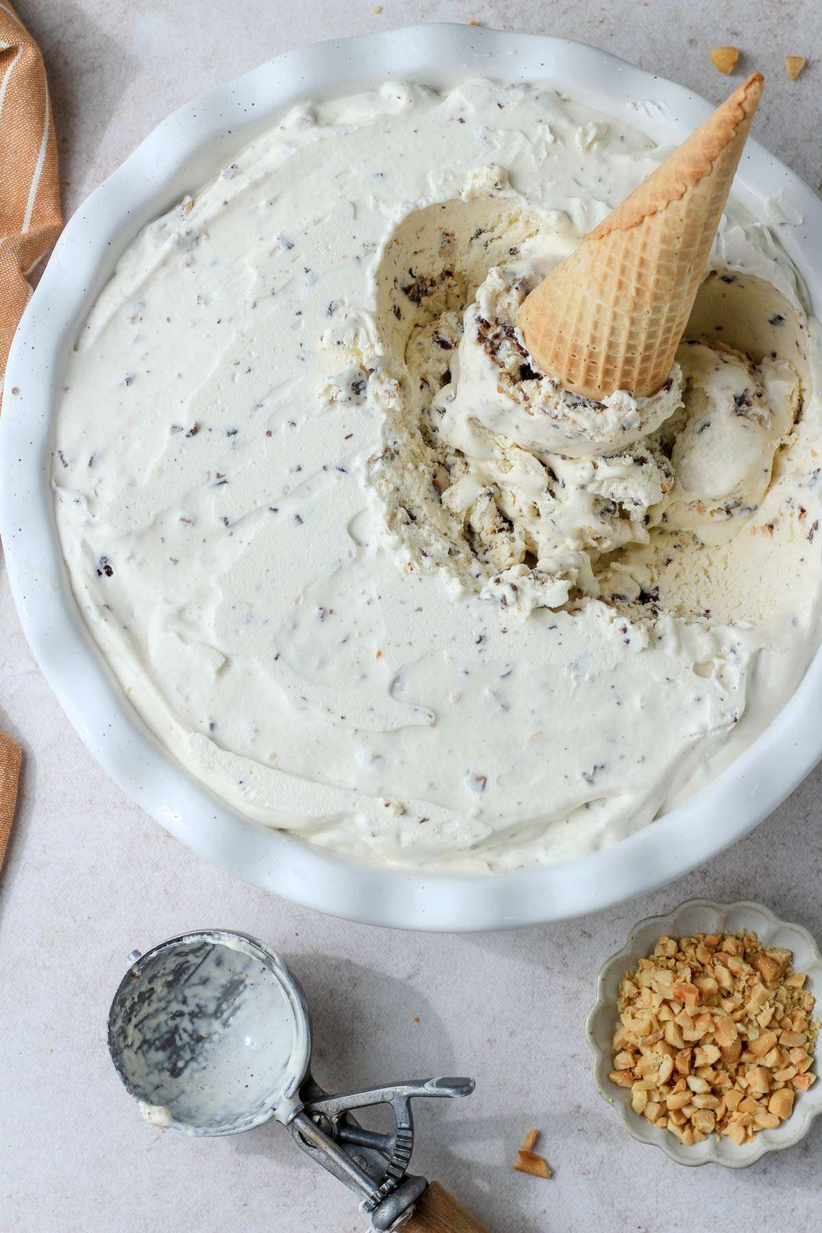 Drumstick ice cream in a white pie pan with an ice cream cone sticking out of the pan and an ice cream scoop to the bottom left of the pan.