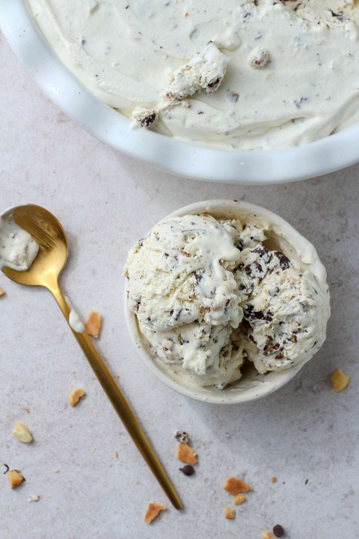 A small white bowl of drumstick ice cream with a gold spoon to the left of the bowl and the ice cream dish in the top right.
