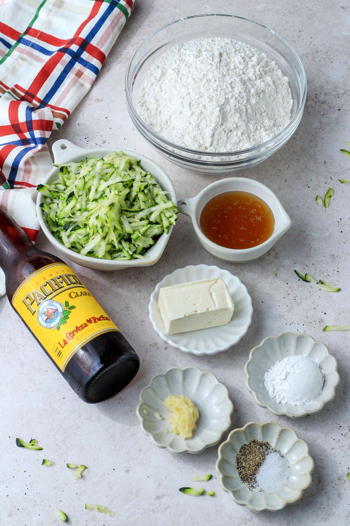 Ingredients for zucchini beer bread on a white counter with a dish towel to the left.