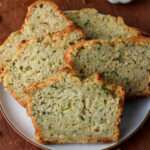 A white plate with five slices of dairy-free zucchini beer bread on a wooden cutting board.