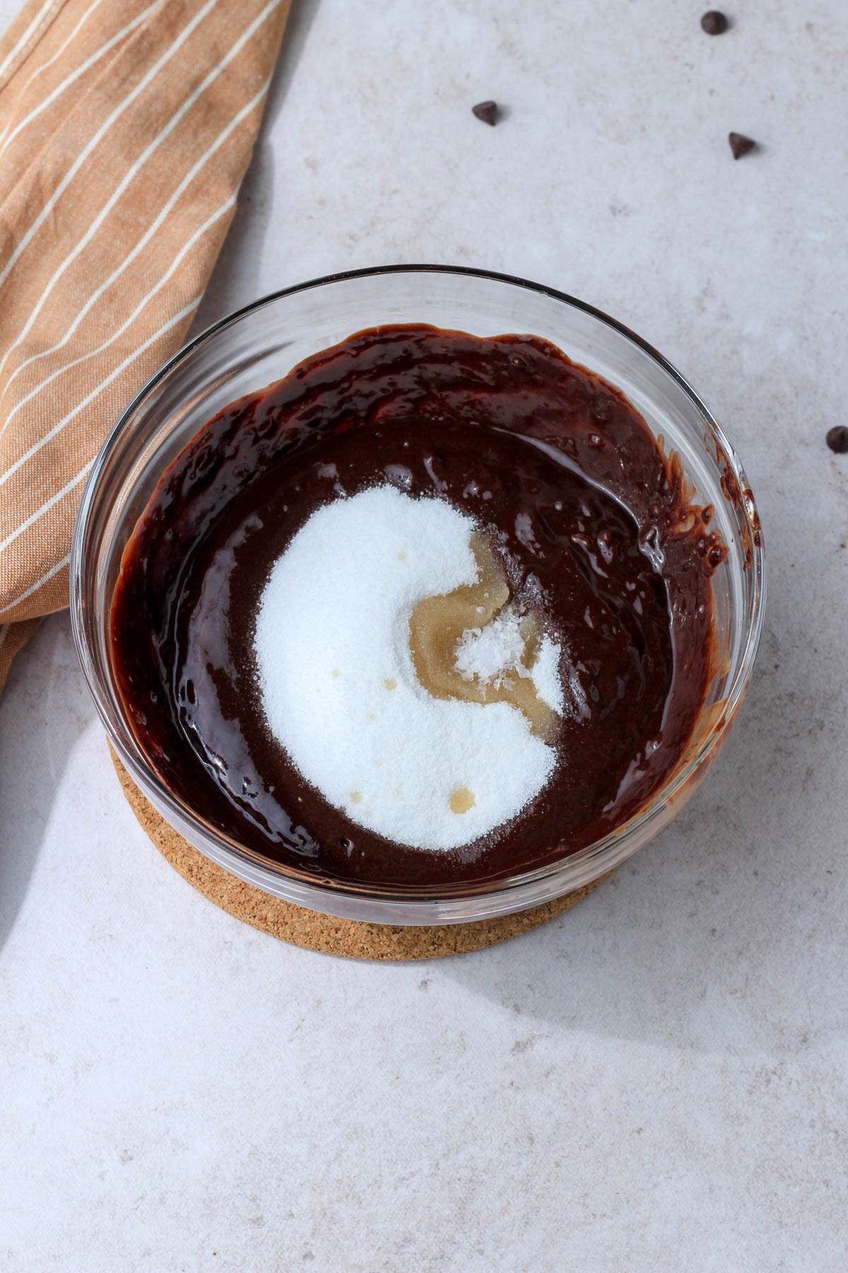 A glass mixing bowl with dairy-free brownie batter topped with sugar and vanilla.