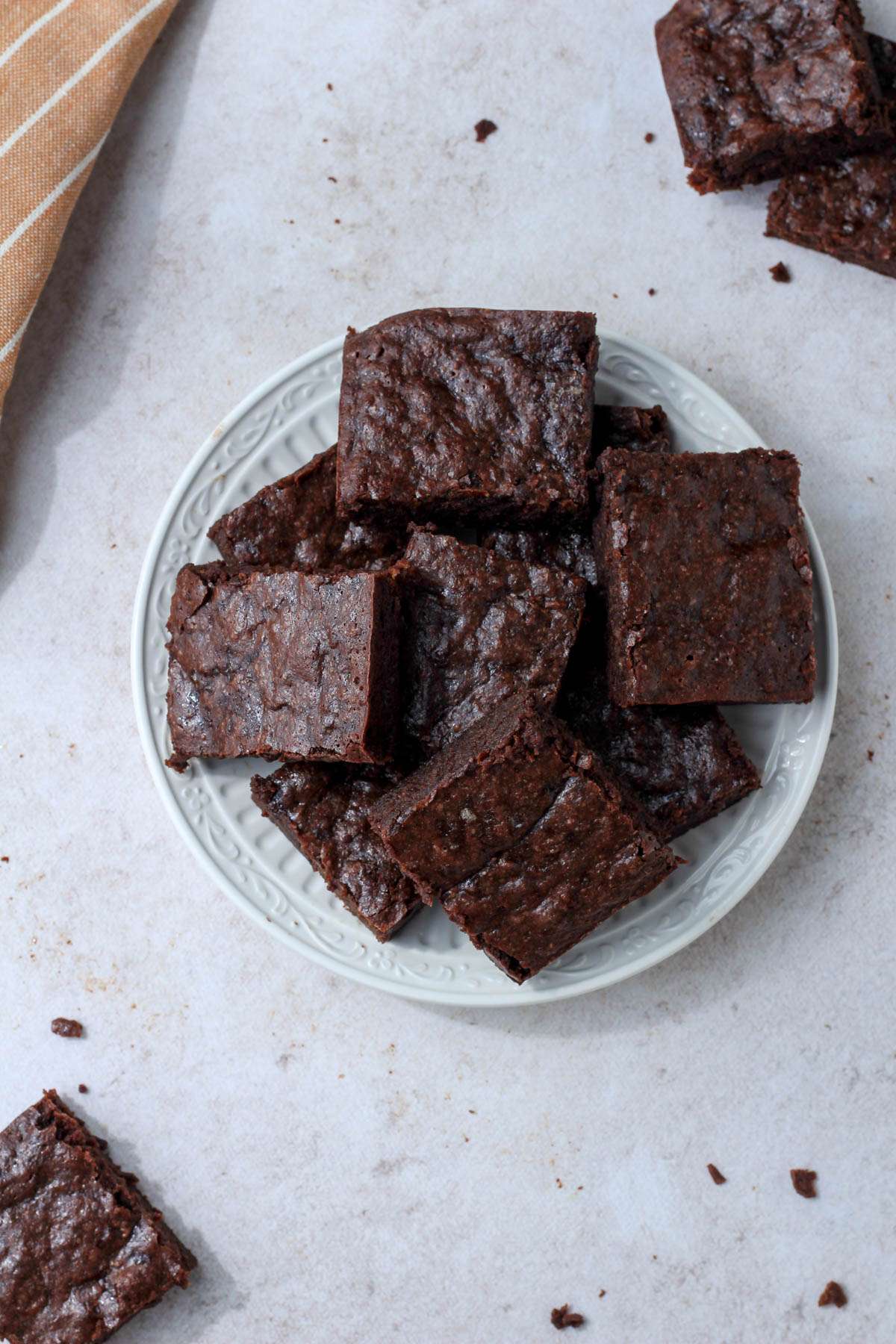 A white plate with a pile of dairy-free brownies on a tan counter.