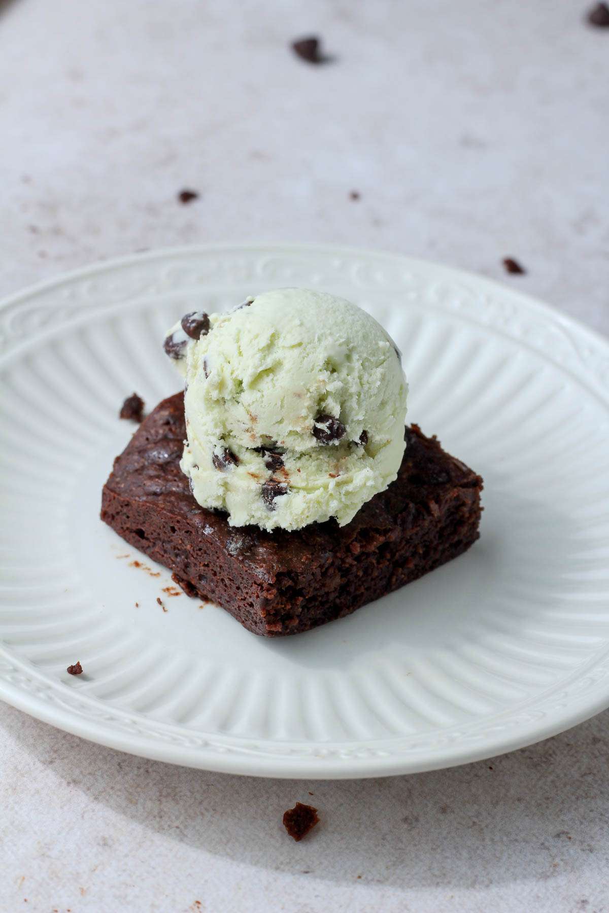 A small white plate with a brownie topped with mint chocolate chip ice cream.