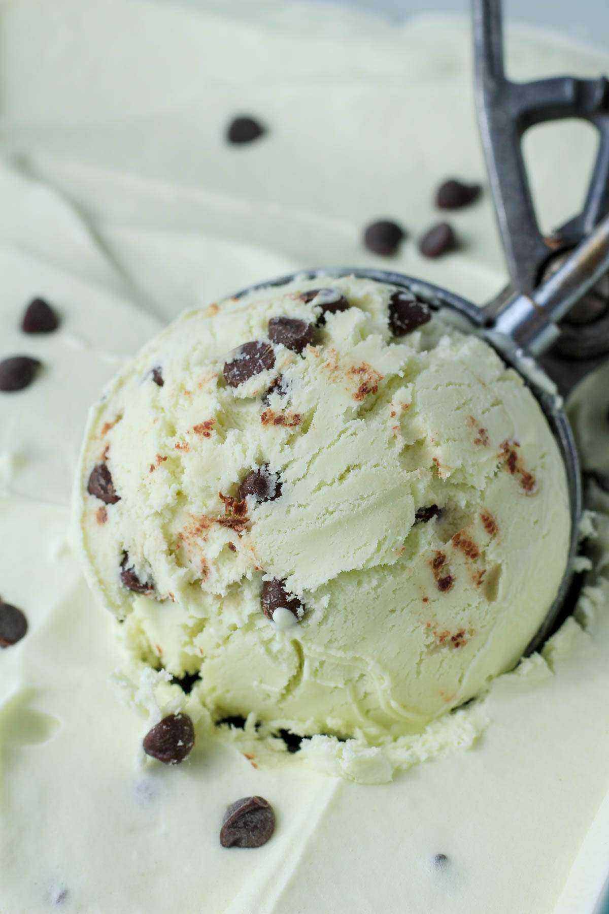 A silver ice cream scoop in a pan of dairy-free mint chocolate chip ice cream with a large scoop on top.