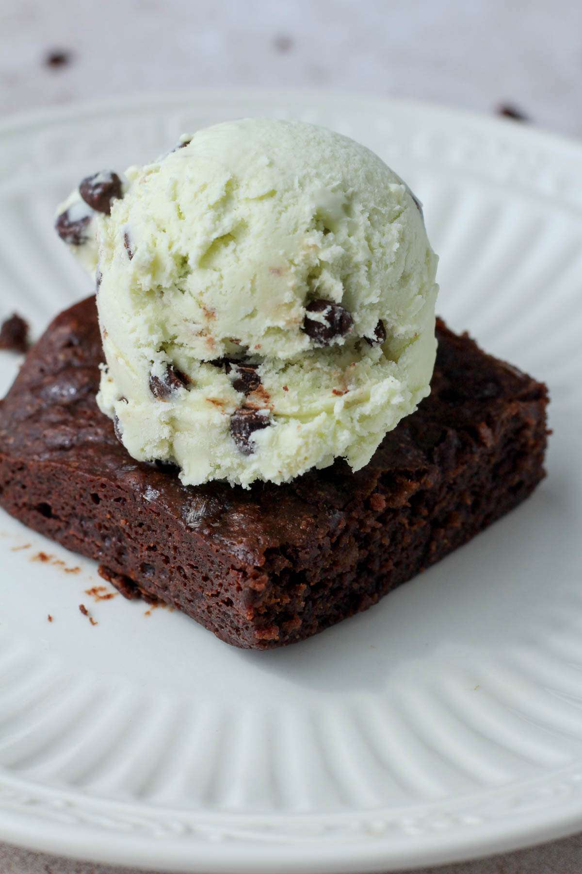 A small white plate with a brownie topped with mint chocolate chip ice cream.