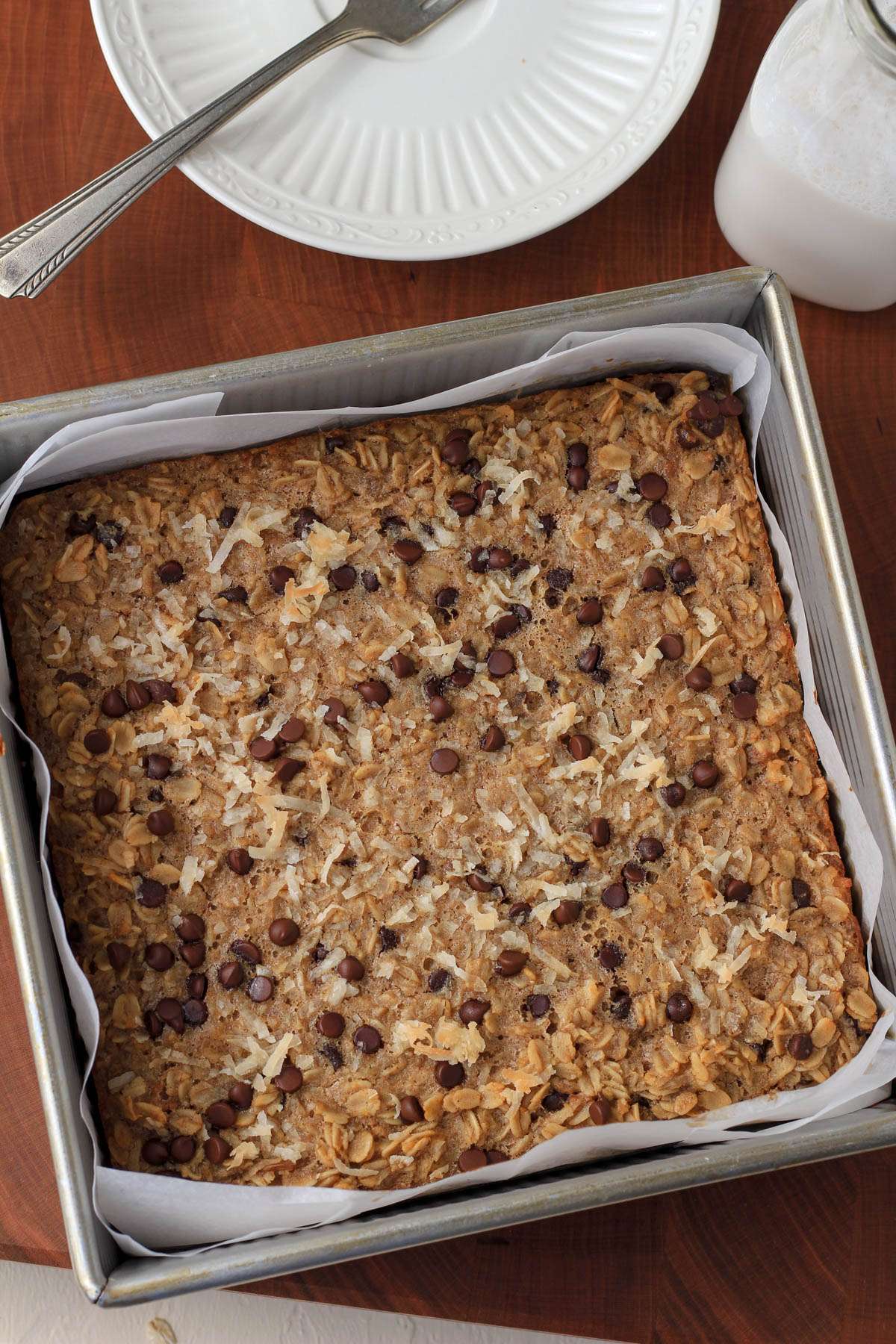 A silver square baking dish with baked almond joy oatmeal bars on a wooden cutting board.