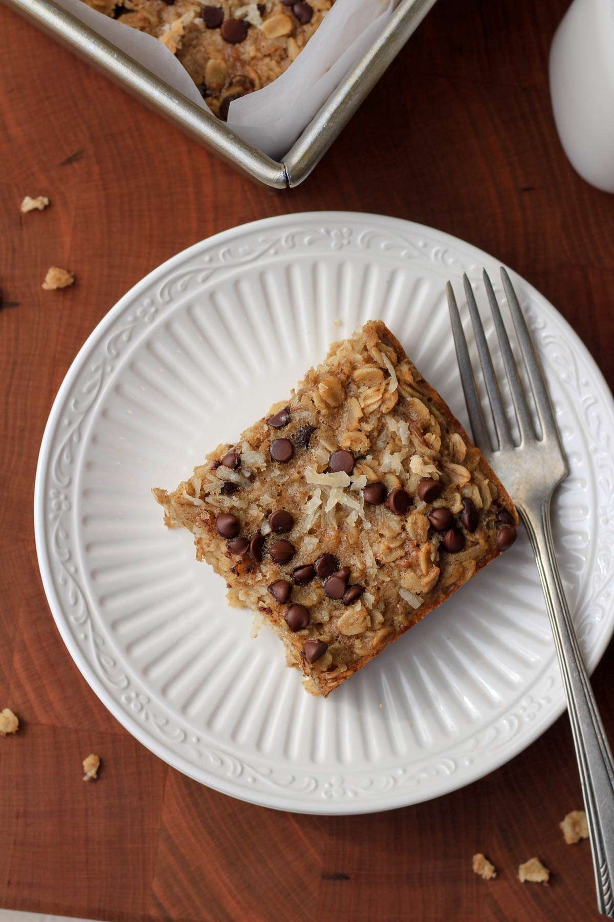 A white plate with a silver fork and a cut square of almond joy baked oatmeal on a wooden counter.