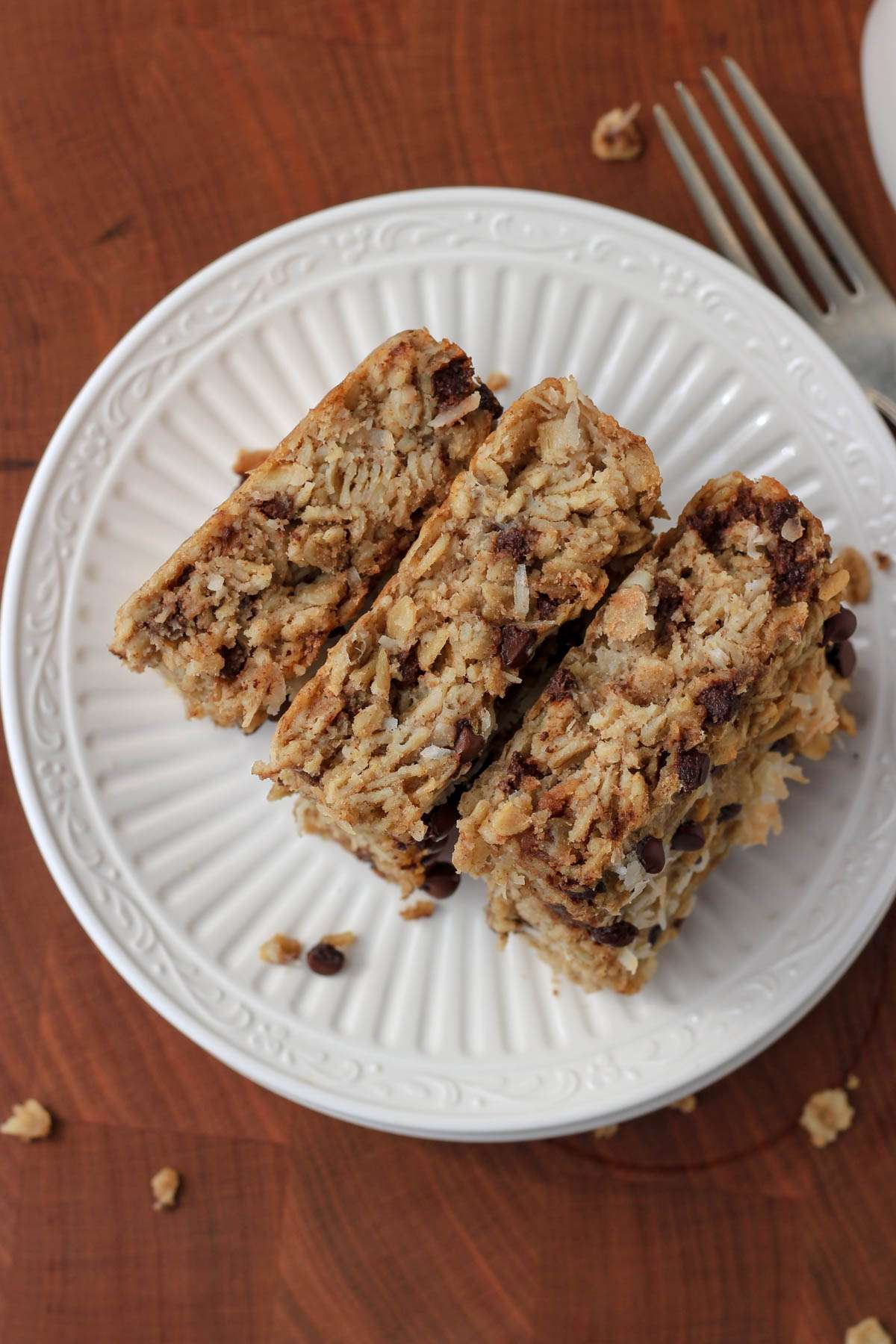 Three cut squares of almond joy baked oatmeal bars on a white plate with a silver fork to the right.