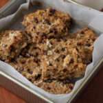 A close up of a square baking pan with parchment paper and cut squares of almond joy baked oatmeal.