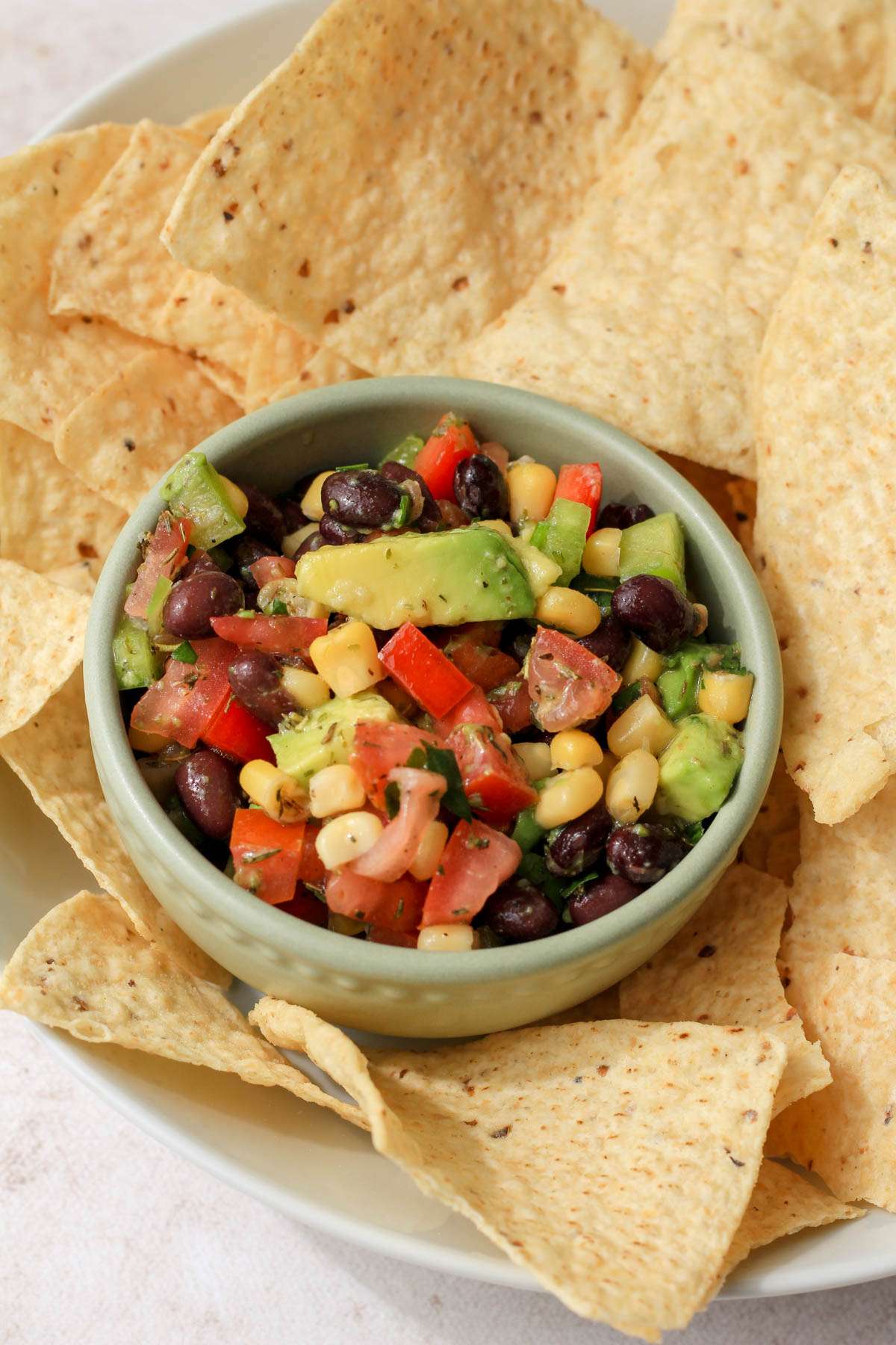 A small green bowl of Texas caviar in a larger white bowl of tortilla chips.