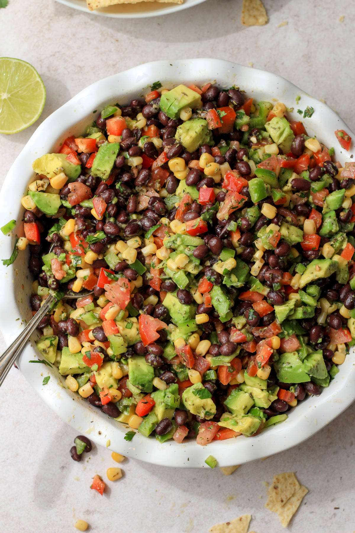 A top down of a deep dish of black bean, corn, and tomato salsa on a tan counter.