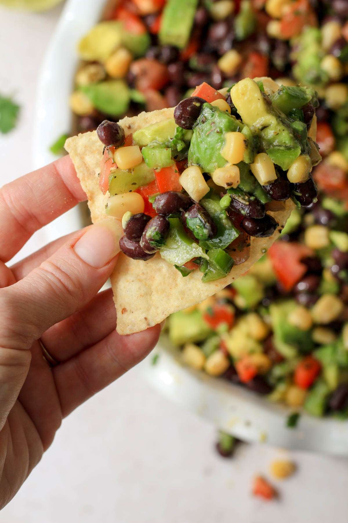A hand holding a tortilla chip with a scoop of Texas caviar.