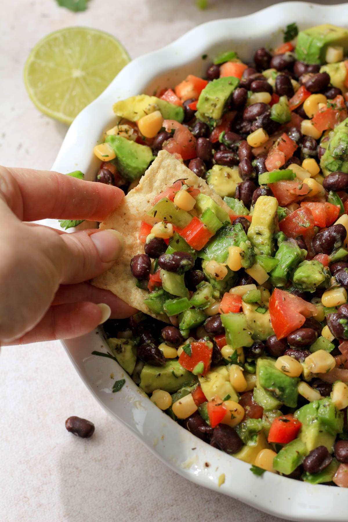 A white pie dish filled with Texas caviar and a hand scooping the Texas caviar from the left with a tortilla chip.