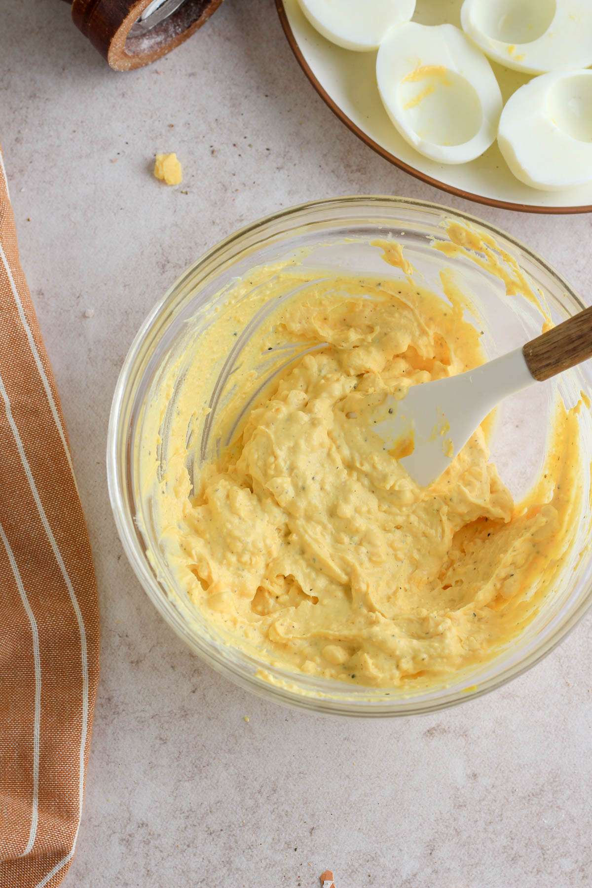 A small glass bowl with a rubber spatula after mixing the deviled egg filling together.