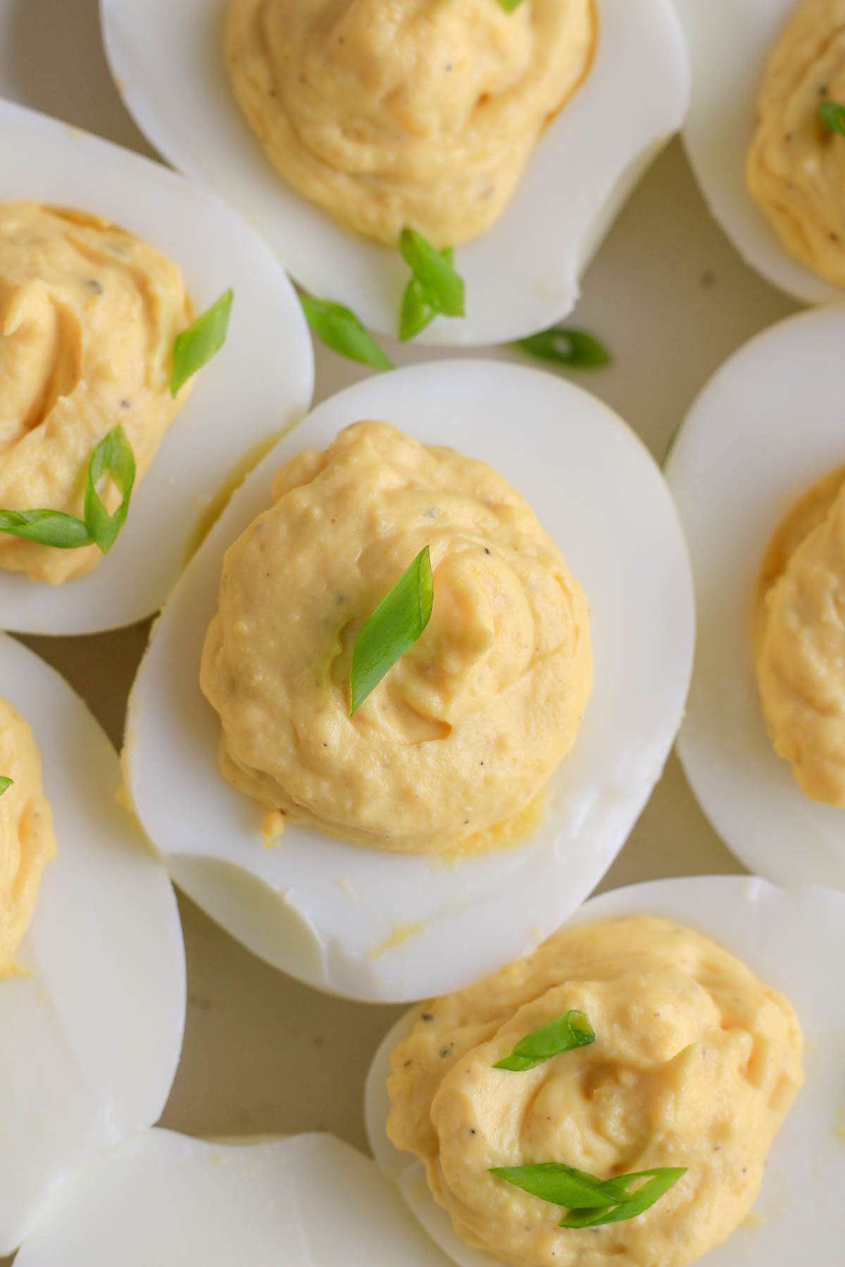 A close up of a classic deviled eggs on a white plate with green onion on top.
