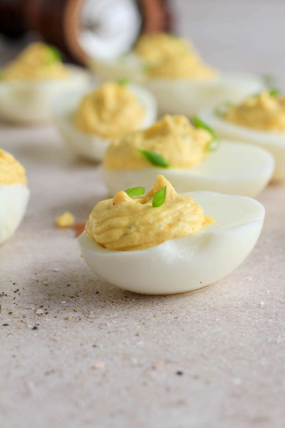 From the side, a classic deviled egg topped with green onion on a tan counter.