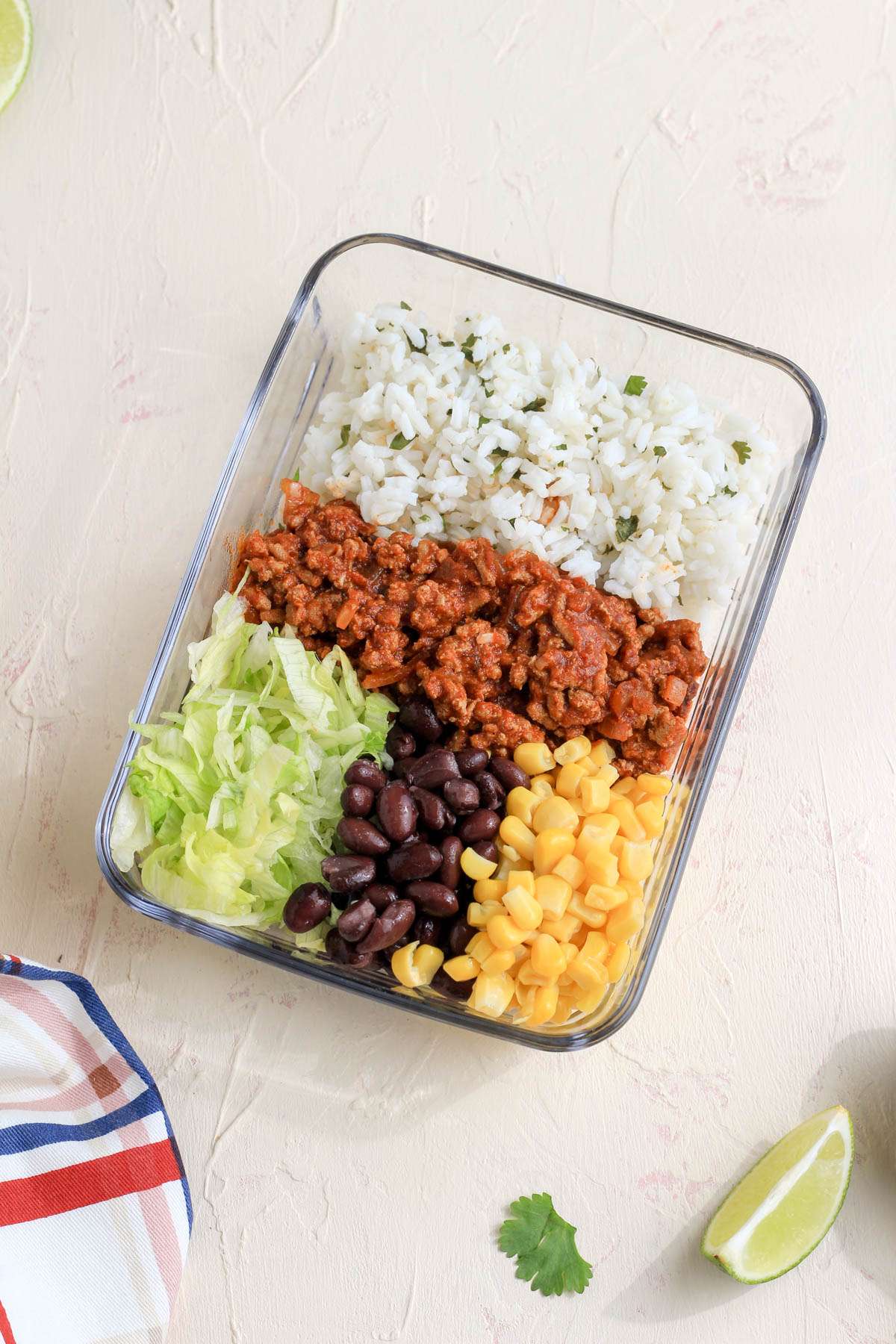A glass pyrex with cilantro lime rice, ground turkey taco meat, shredded lettuce, black beans, and corn.
