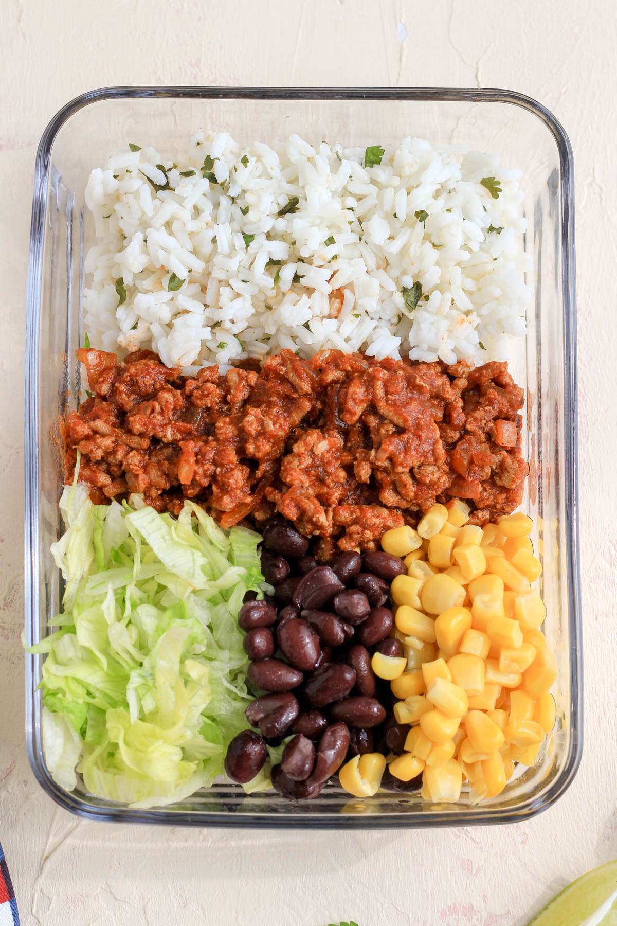 A top down of a meal prep container with cilantro lime rice, ground turkey taco meat, shredded lettuce, black beans, and corn.