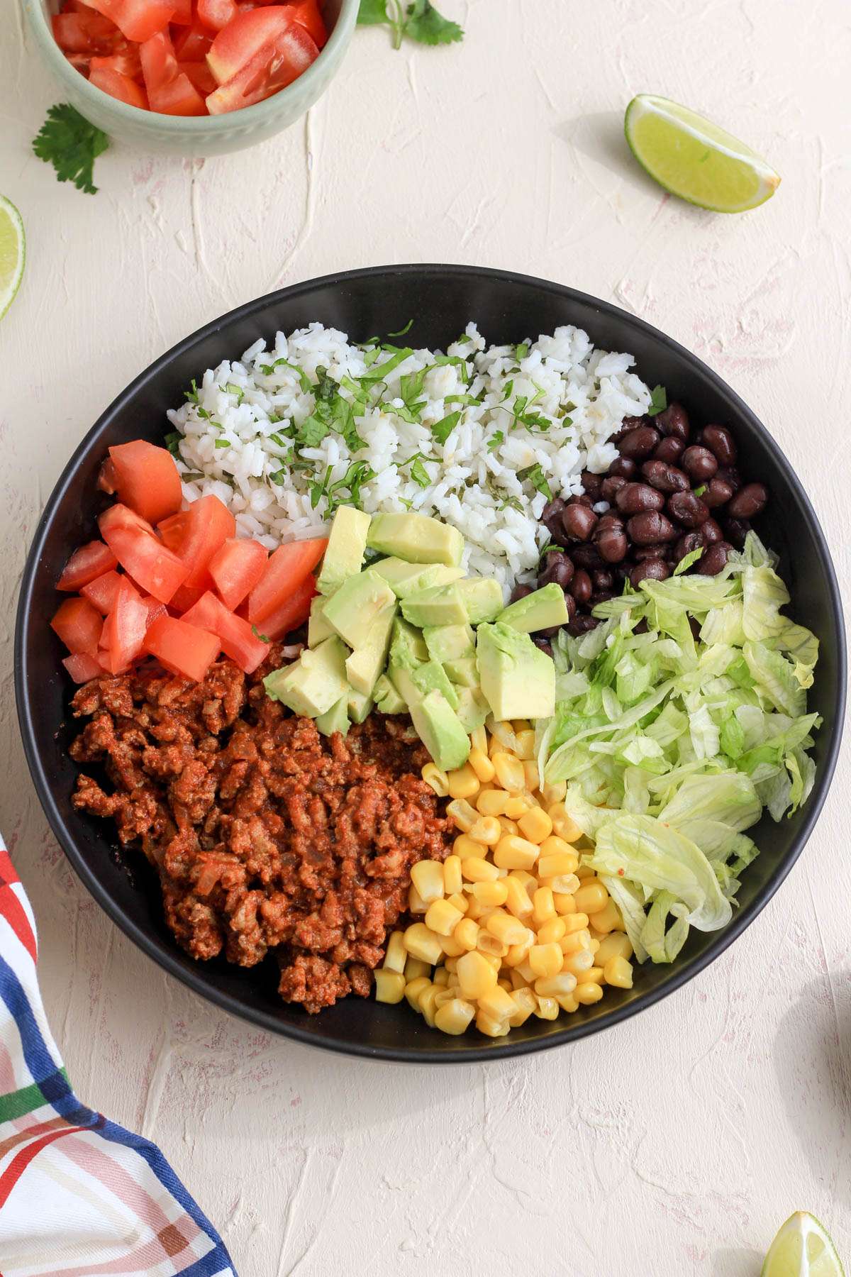 A top down image of a turkey taco lunch bowl topped with added chopped tomatoes and avocado.