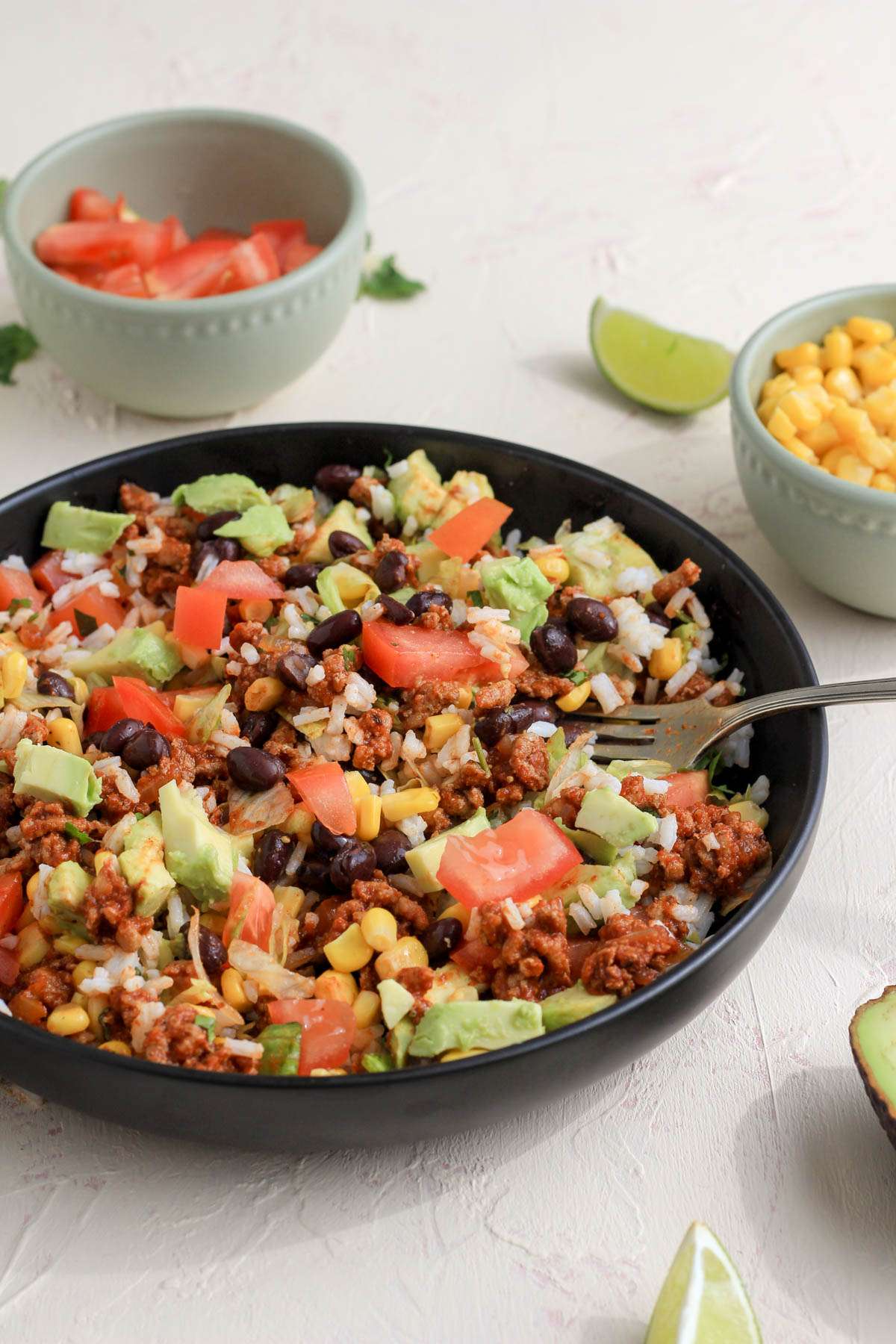 A turkey taco meat style burrito bowl in a shallow black bowl with a silver fork on the right side.