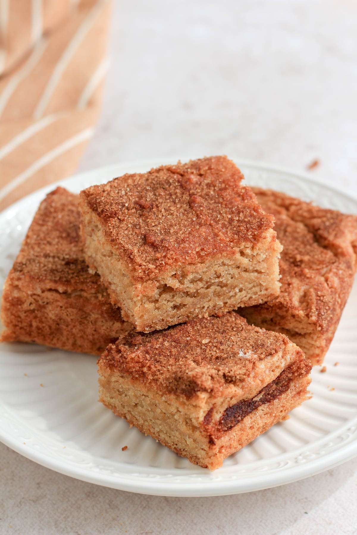 A small white plate topped with three moist snickerdoodle cookie bars on a tan counter.