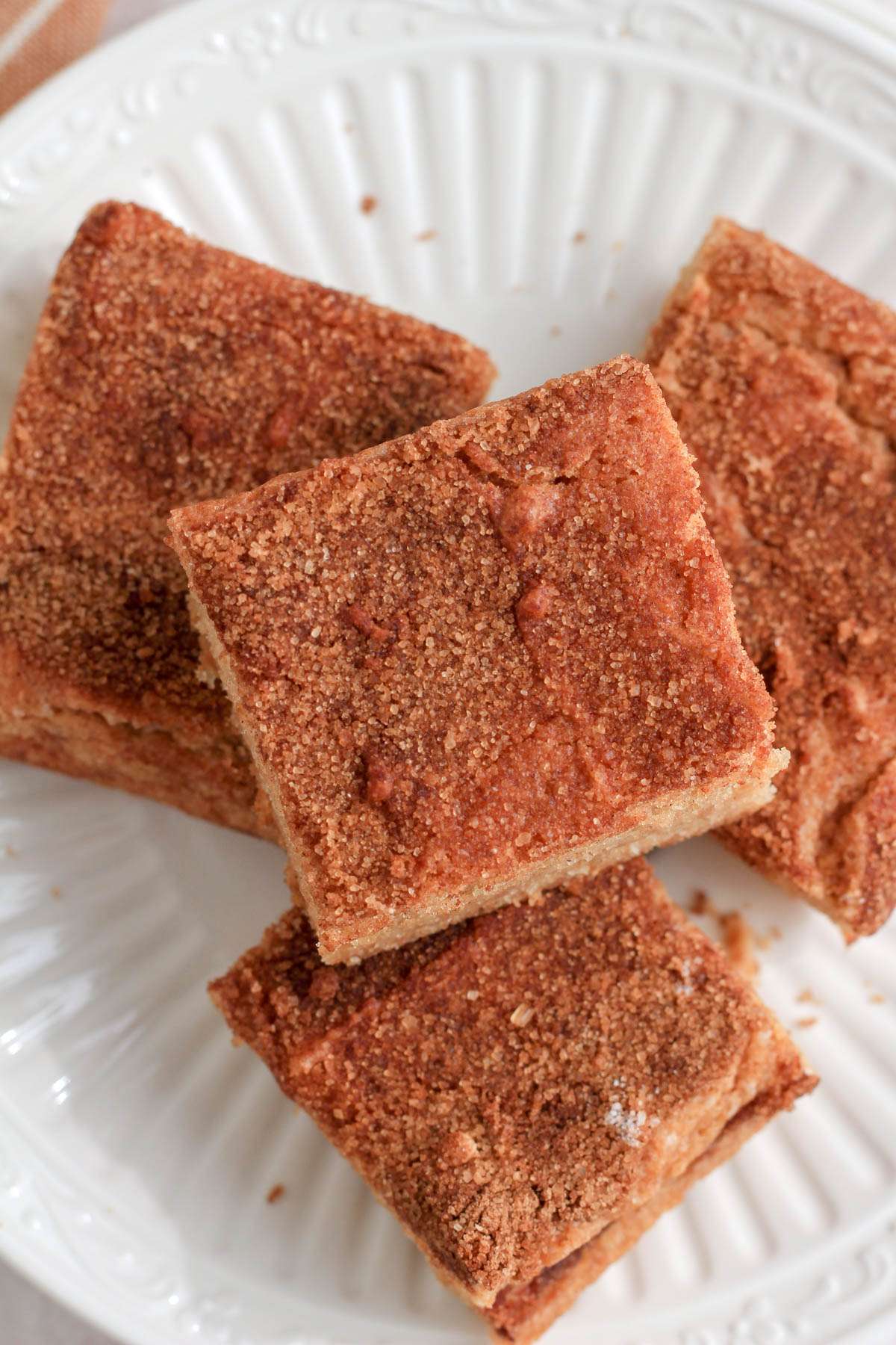 A top down image of snickerdoodle cookie bars stacked on a small white plate with some crumbs.