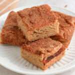 A small white plate with four snickerdoodle cookie bars stacked in the middle.
