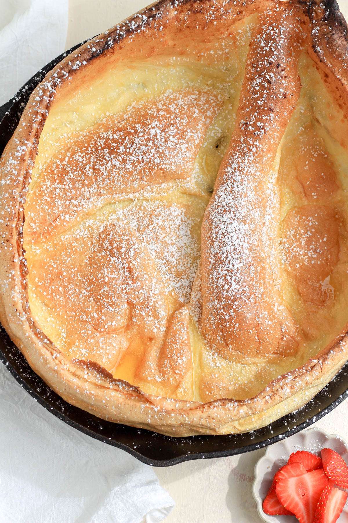 A dairy-free dutch baby in a black cast iron skillet dusted with powdered sugar.