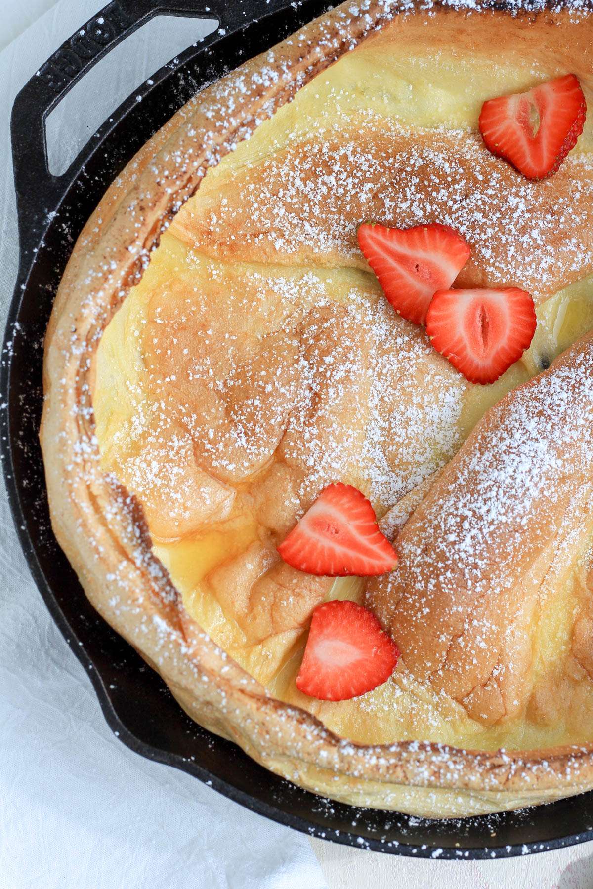The left side of a dairy-free dutch baby topped with powdered sugar and sliced strawberries.