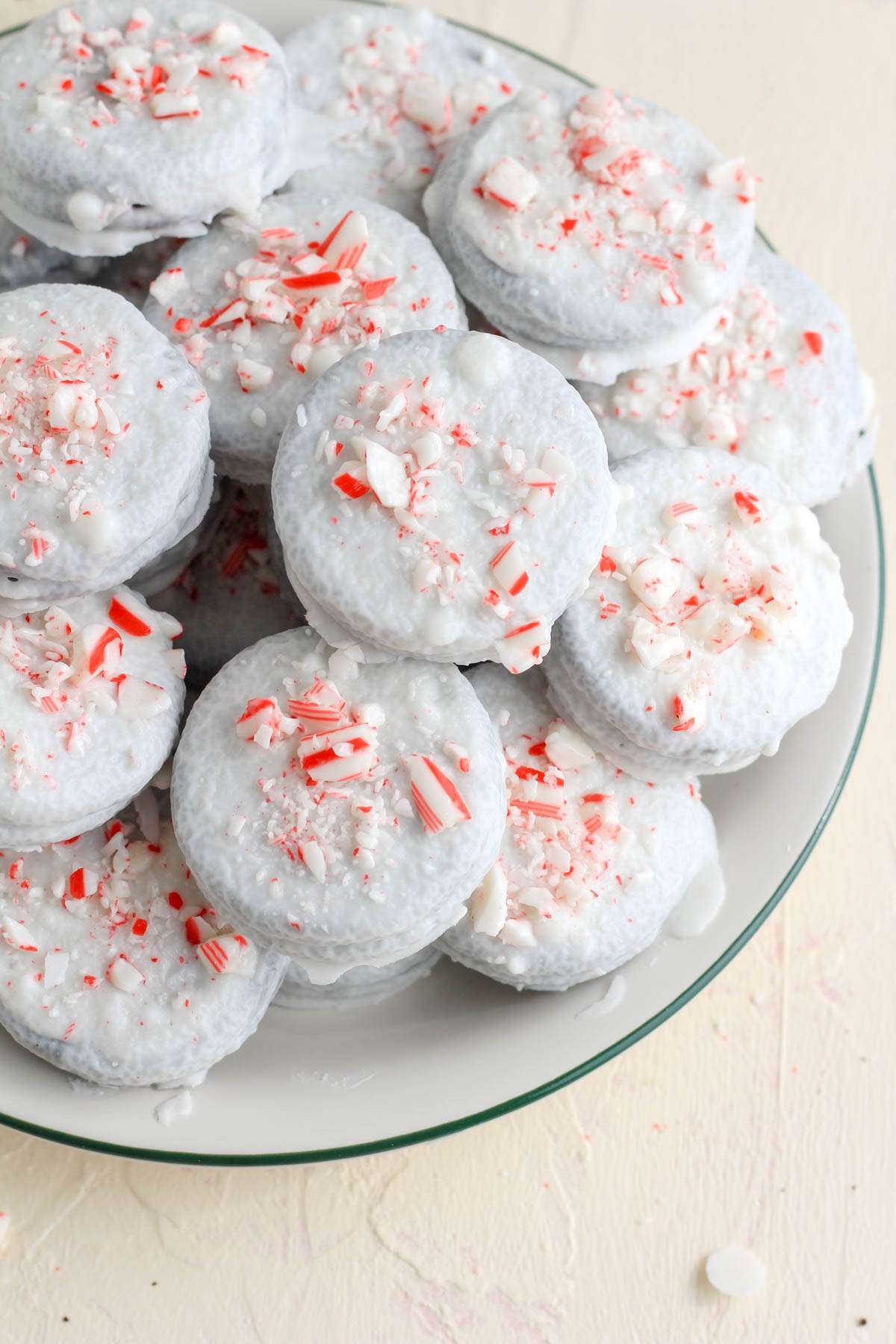 A green rimmed plate with a pile of vegan peppermint chocolate dipped oreos.