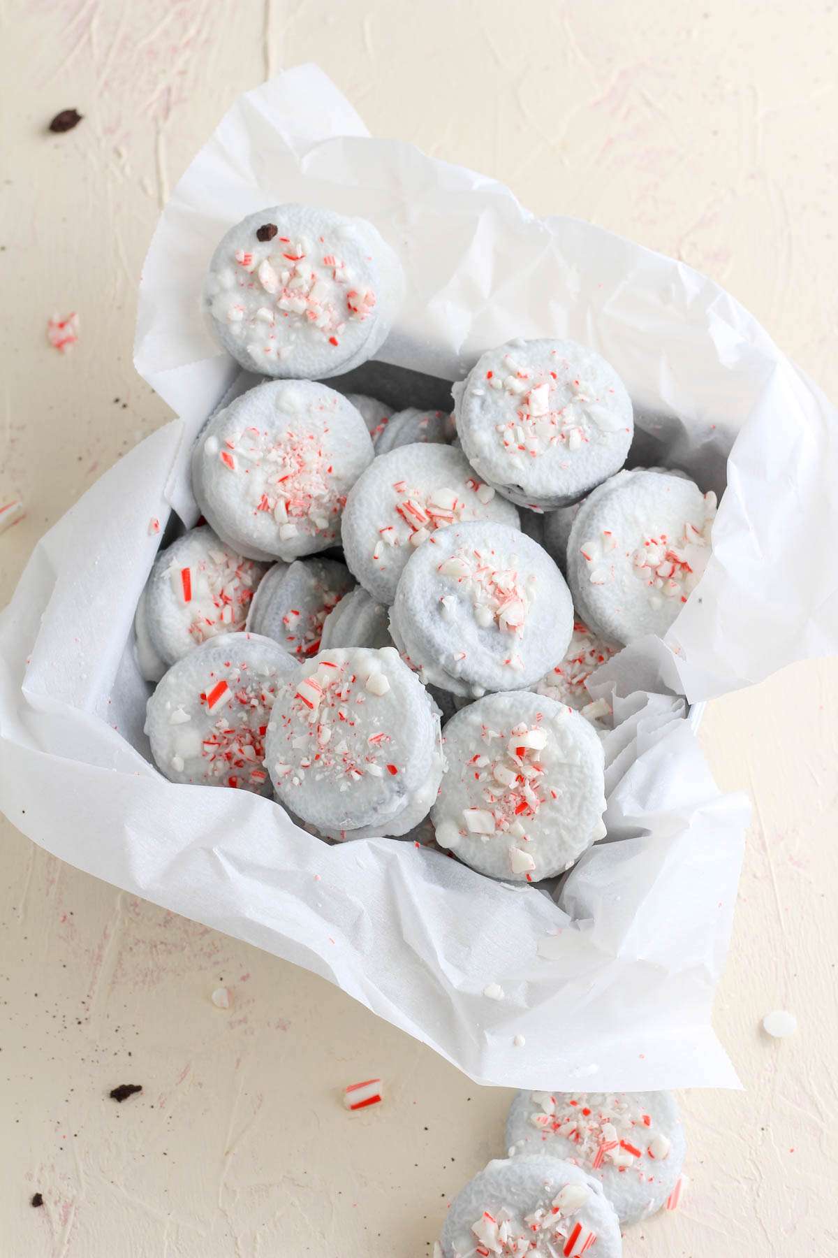 Peppermint white chocolate oreos in a parchment paper lined cookie tin on a cream counter.