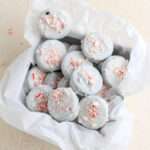 A close up of candy cane topped peppermint white chocolate oreos in a parchment paper lined cookie box.