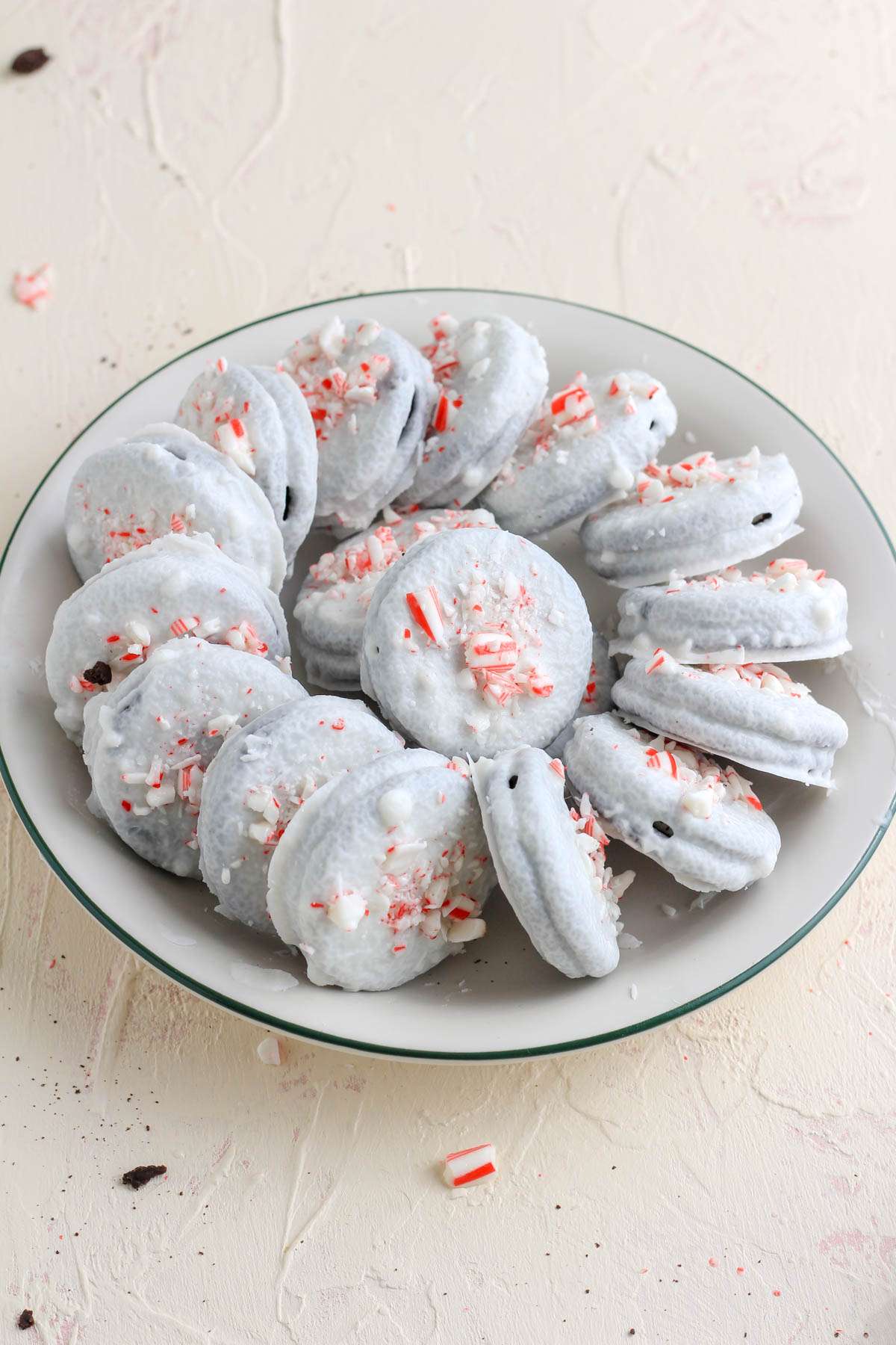 From the side view of a cream plate with a green rim topped with vegan peppermint white chocolate dipped oreo cookies.