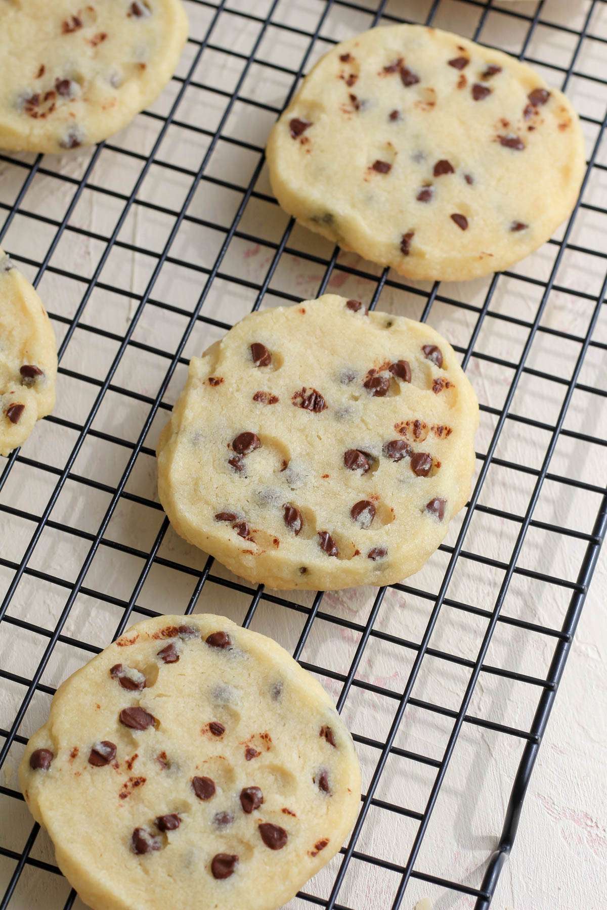A cream counter with a cooling rack topped with vegan chocolate chip cookies.