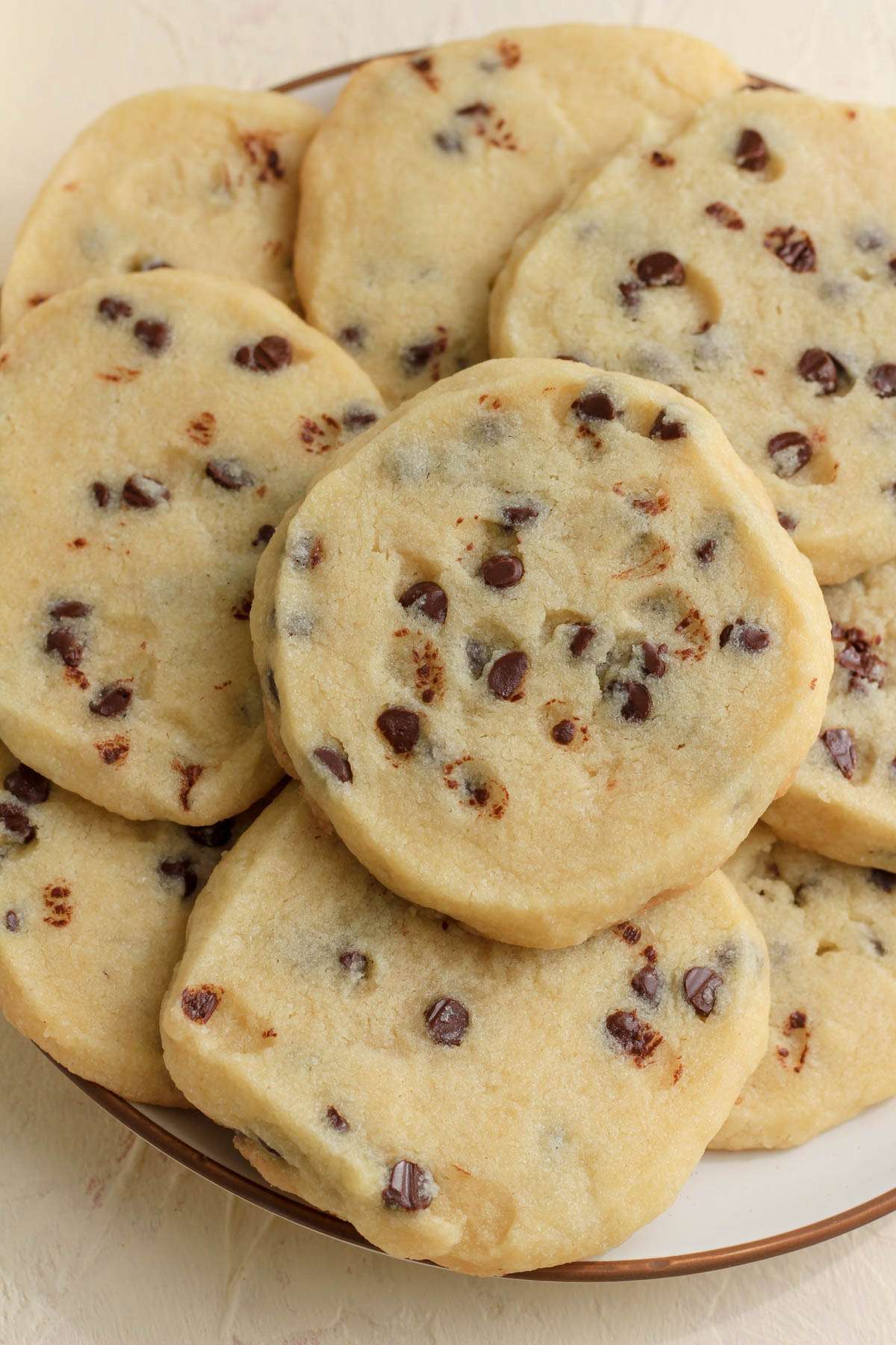 A white plate with brown rim topped with vegan chocolate chip cookies on a cream counter.