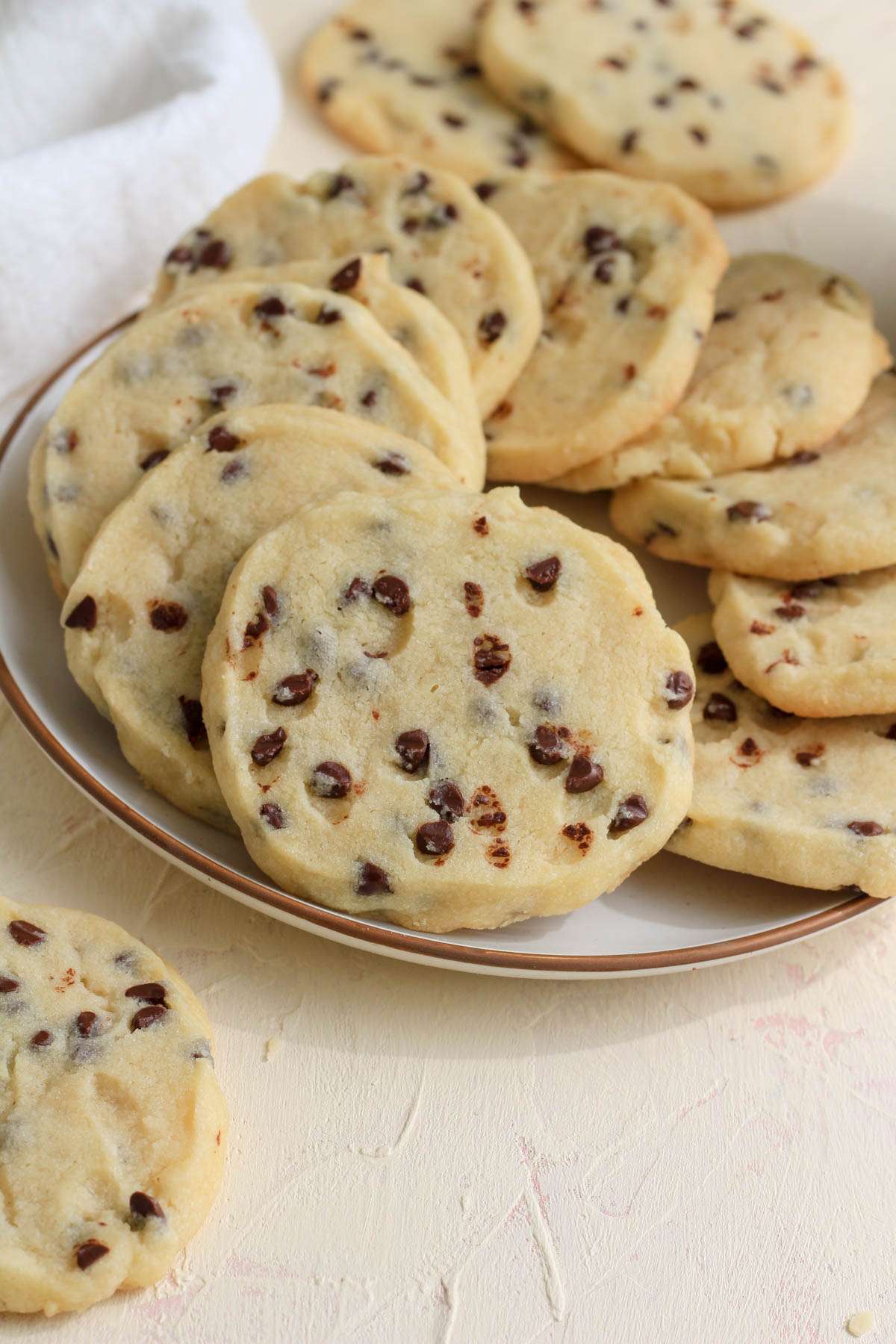 Vegan shortbread cookies on a white and tan plate with a few on the cream counter in front of the plate.