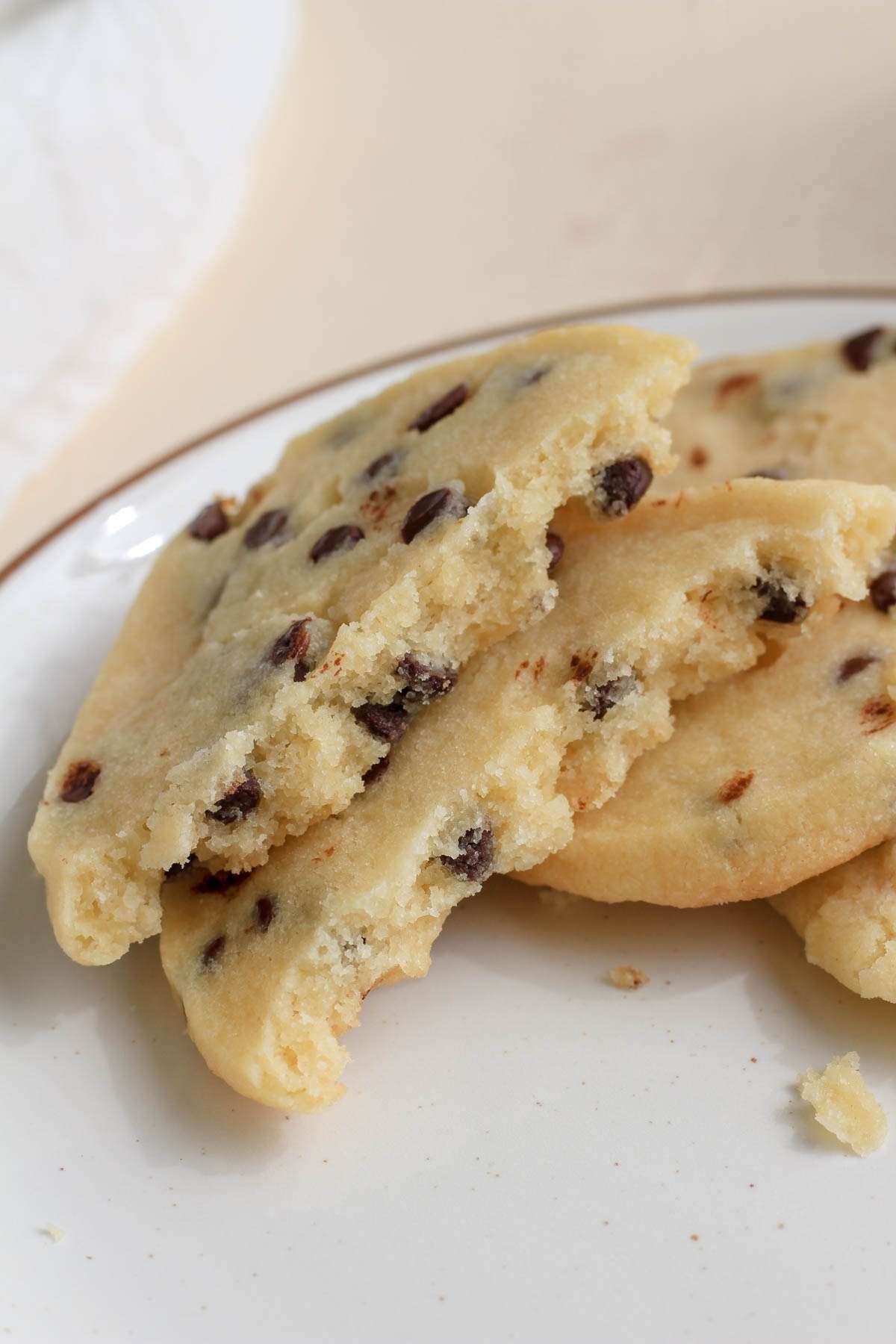 A broken shortbread cookie with vegan chocolate chips on a white plate with a brown rim.