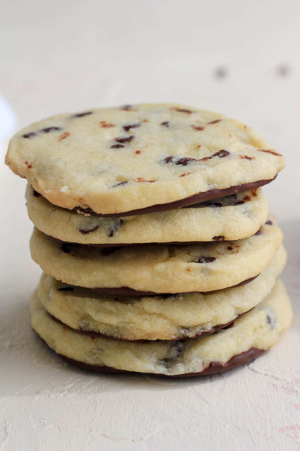 A stack of vegan chocolate chip shortbread cookies coated with dairy-free chocolate on the bottom of the cookie.
