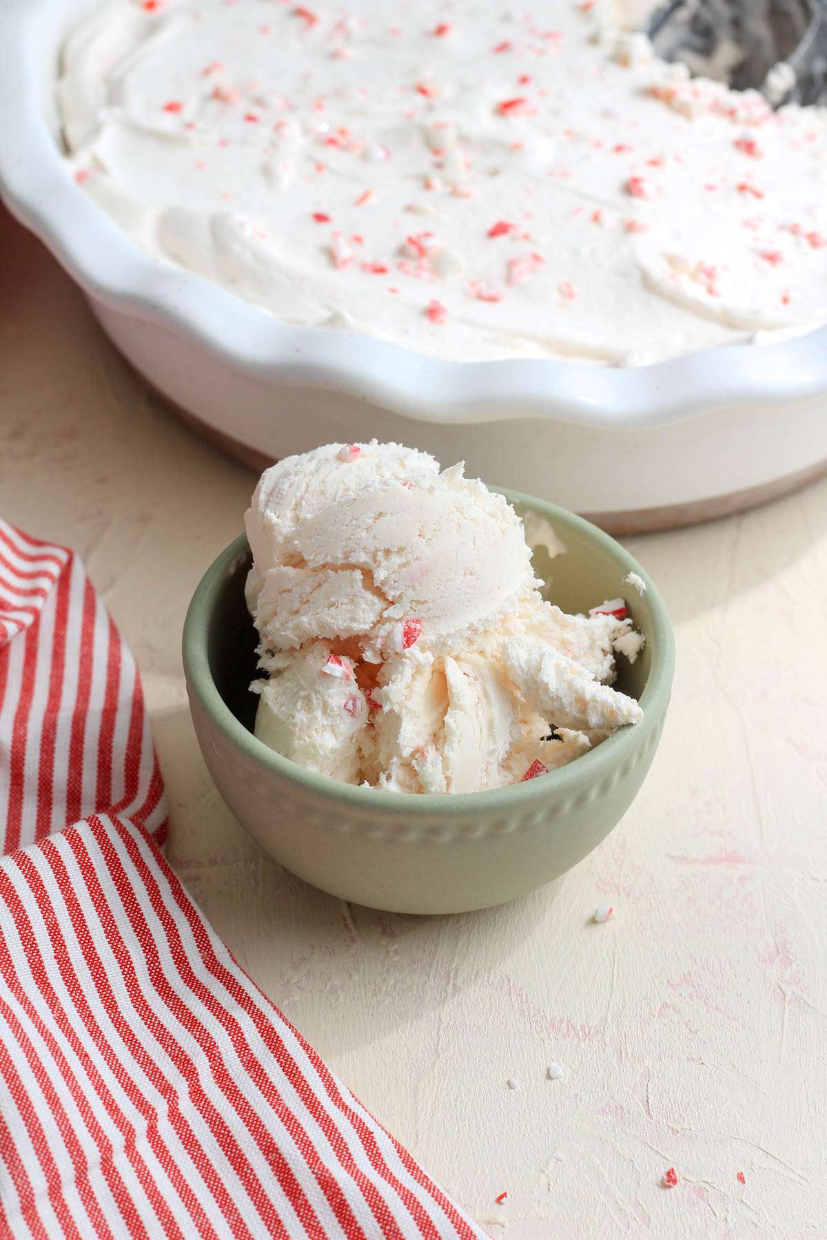 A small green bowl filled with vegan no churn peppermint ice cream on a cream counter with a white pie pan of ice cream in the back.