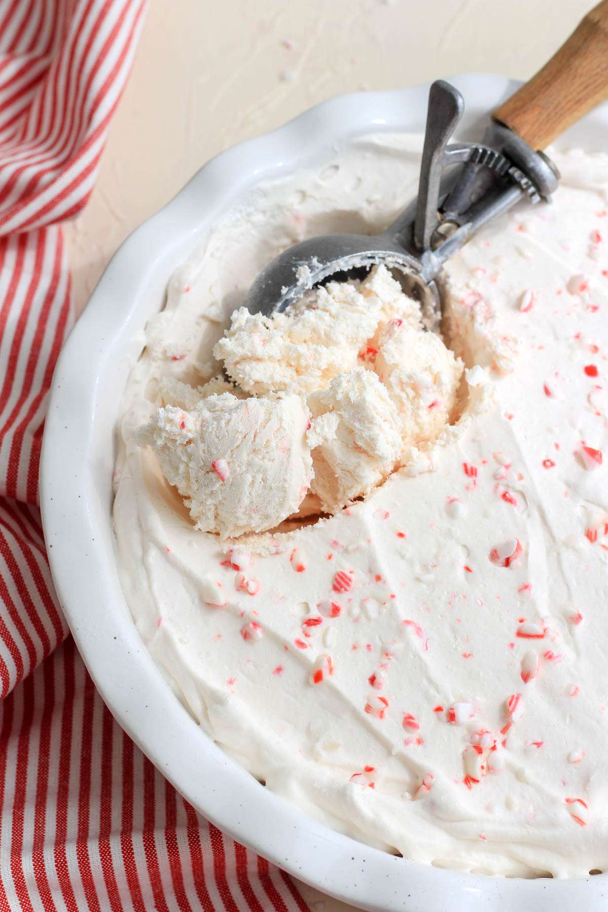 A white pan of vegan peppermint ice cream with a silver and wooden ice cream scoop in the pan.